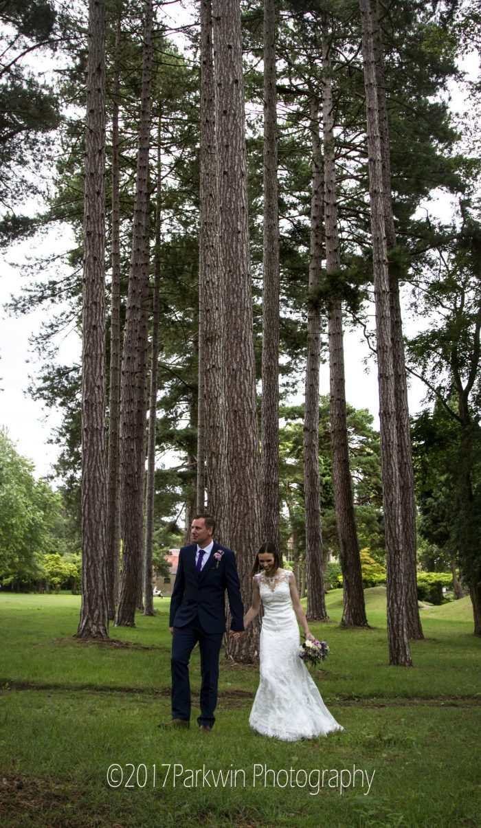 bride and Groom walking hrough trees at Fanhams Hall